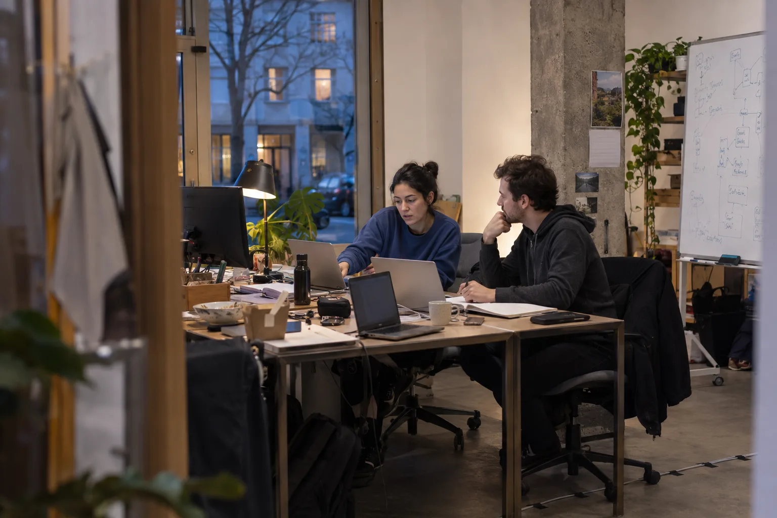 Illustrative scene: two founders discussing their work in a small startup office at dusk.
